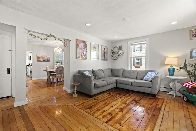 living room with baseboard heating, baseboards, a notable chandelier, and a healthy amount of sunlight