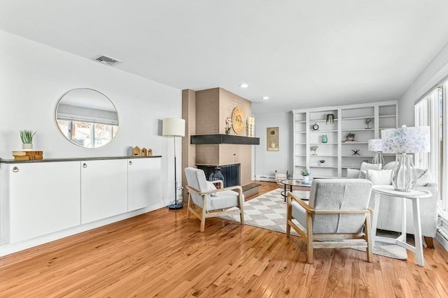 sitting room featuring baseboards, visible vents, light wood-style floors, a brick fireplace, and recessed lighting