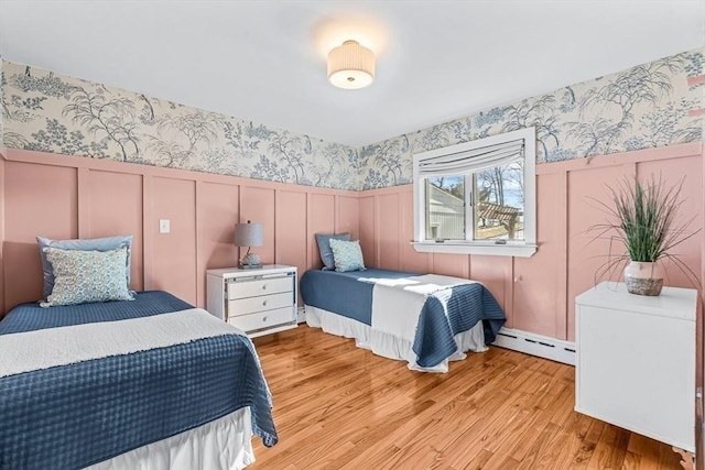 bedroom with wallpapered walls, light wood finished floors, a wainscoted wall, a baseboard heating unit, and a decorative wall