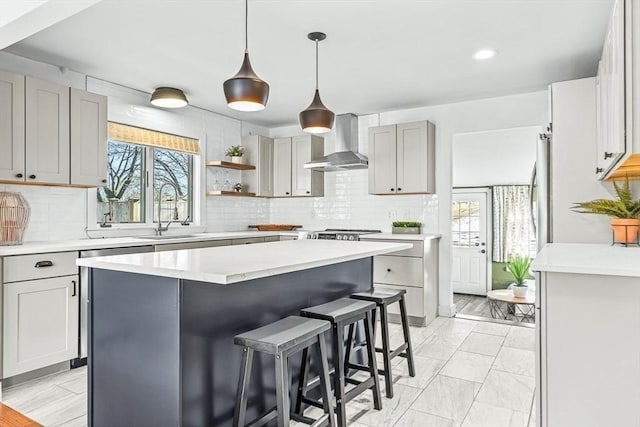 kitchen featuring decorative backsplash, a breakfast bar area, light countertops, wall chimney range hood, and a sink