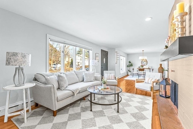 living area featuring baseboard heating, a brick fireplace, light wood finished floors, and recessed lighting