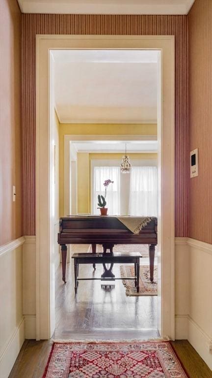 corridor featuring wallpapered walls, wood finished floors, and a wainscoted wall