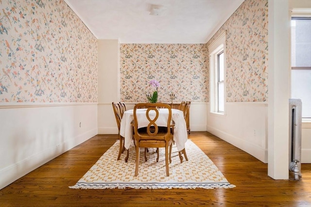 dining room with wallpapered walls, wood finished floors, and wainscoting