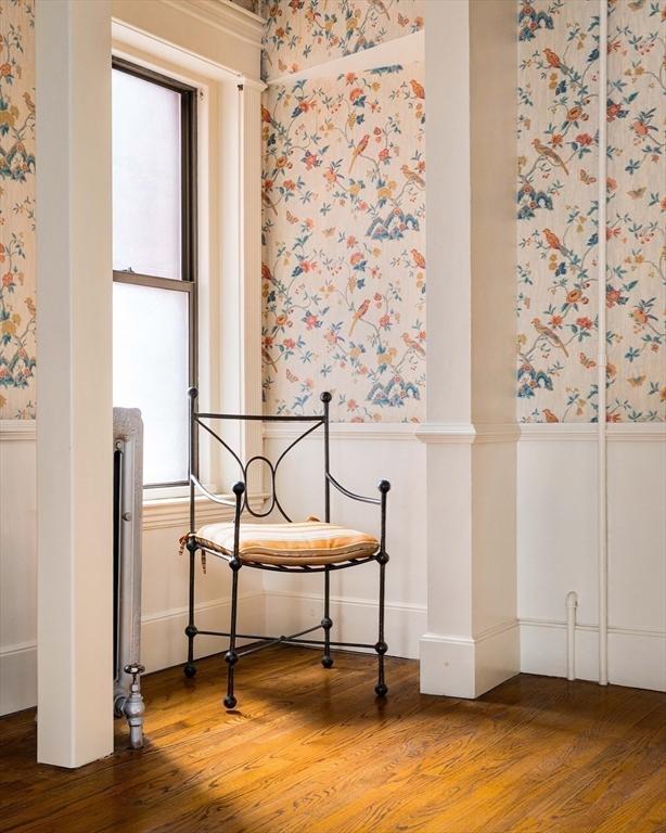 interior space featuring a wainscoted wall, wallpapered walls, ornate columns, and wood finished floors