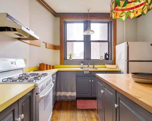 kitchen with under cabinet range hood, a sink, dark wood-style floors, white appliances, and butcher block counters