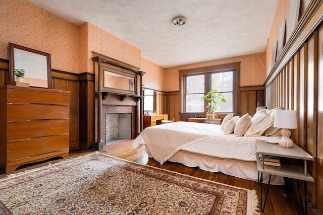 bedroom featuring wallpapered walls, wood finished floors, a wainscoted wall, and a large fireplace