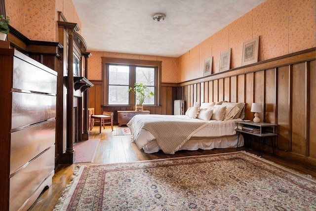 bedroom with wallpapered walls, wainscoting, built in fridge, and hardwood / wood-style floors