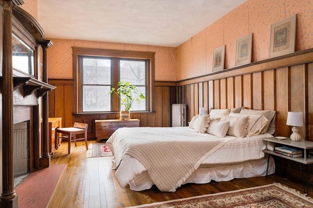 bedroom featuring a wainscoted wall, a fireplace, wallpapered walls, and hardwood / wood-style floors