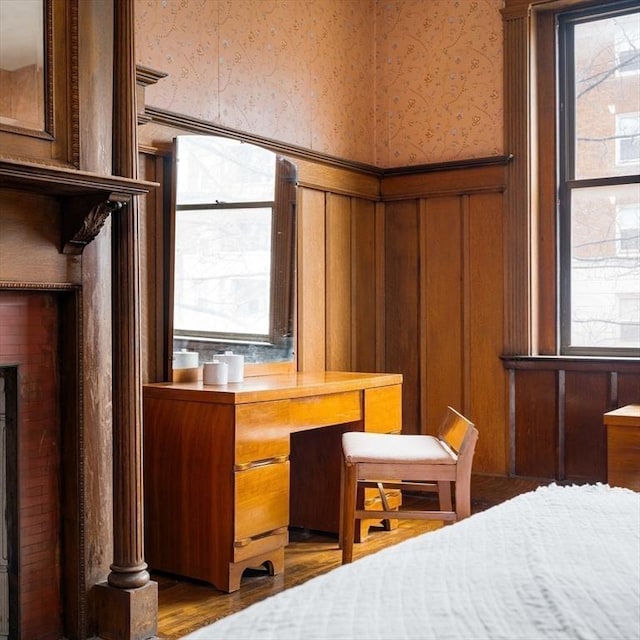 bedroom featuring wood finished floors, wainscoting, wallpapered walls, and multiple windows