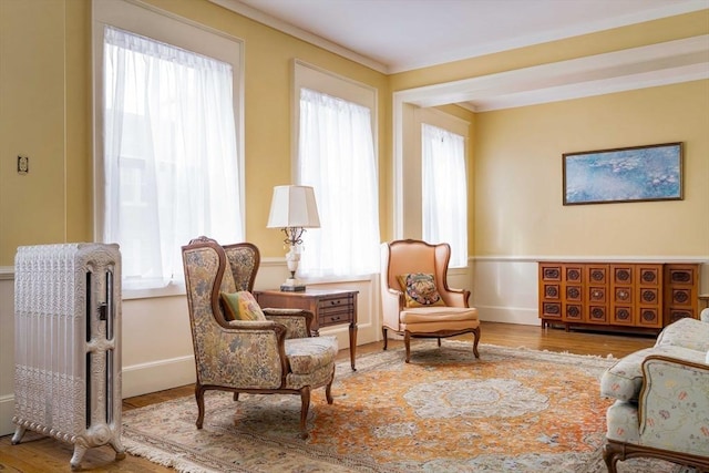 living area with wood finished floors, ornamental molding, and radiator heating unit