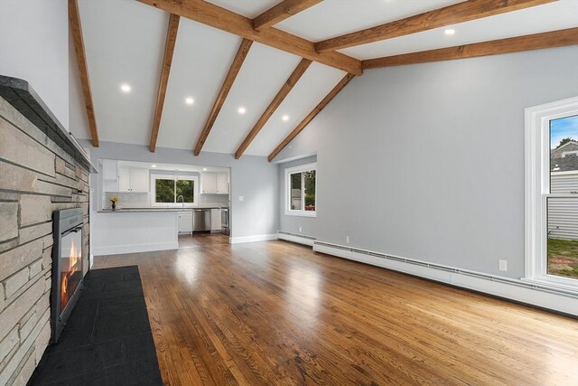 unfurnished living room with wood-type flooring, baseboard heating, beamed ceiling, and a wealth of natural light