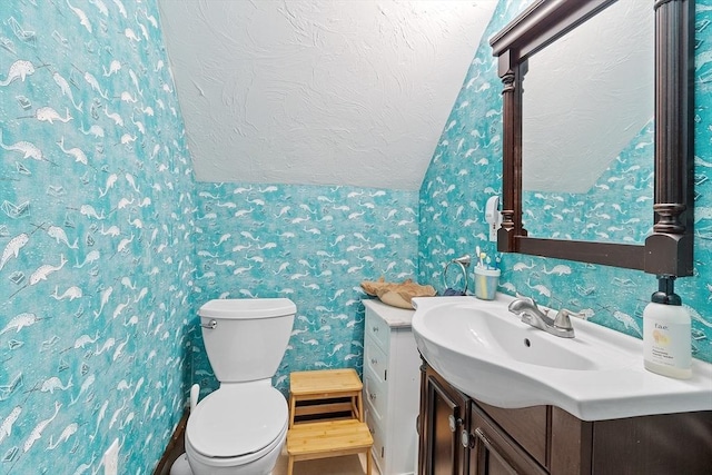 bathroom with wallpapered walls, toilet, vanity, and a textured ceiling