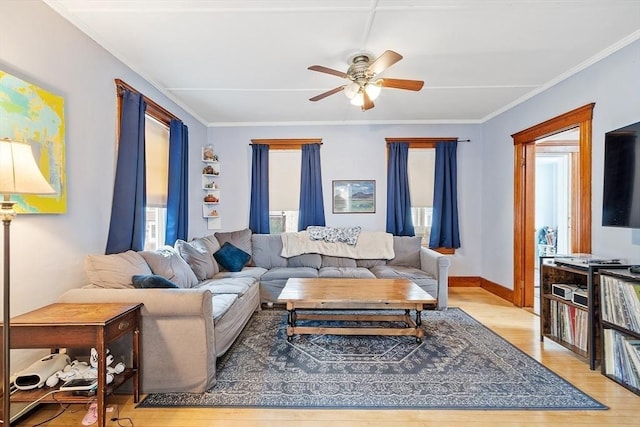 living area with crown molding, light wood-style flooring, baseboards, and a ceiling fan