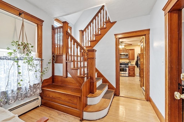 stairs with a baseboard heating unit, a ceiling fan, and hardwood / wood-style flooring