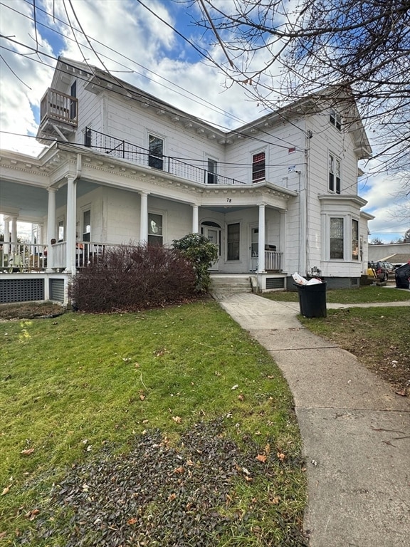 rear view of house with a balcony, a lawn, and covered porch