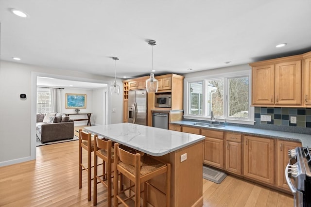 kitchen featuring a breakfast bar area, a sink, a kitchen island, hanging light fixtures, and appliances with stainless steel finishes