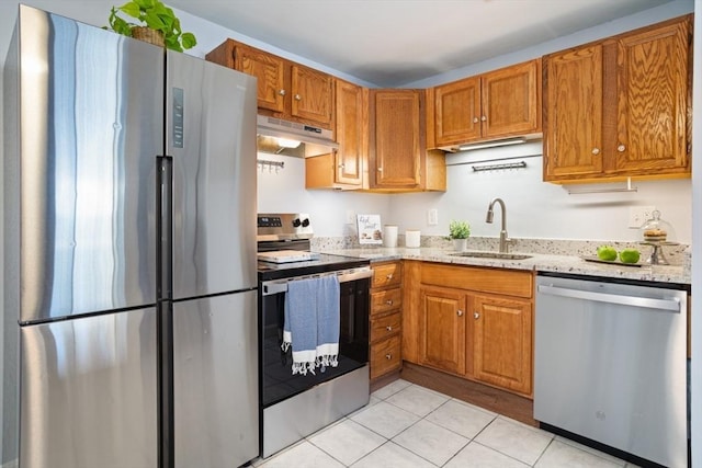 kitchen featuring light tile patterned floors, brown cabinets, stainless steel appliances, under cabinet range hood, and a sink