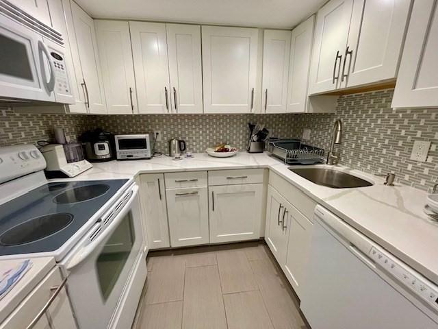 51 John St Unit 201, Brookline, MA 02446 - kitchen with white appliances, white cabinets, decorative backsplash, light tile patterned flooring, and light stone countertops
