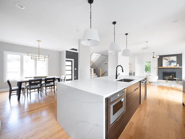 kitchen featuring pendant lighting, sink, light hardwood / wood-style flooring, a kitchen island with sink, and a wealth of natural light