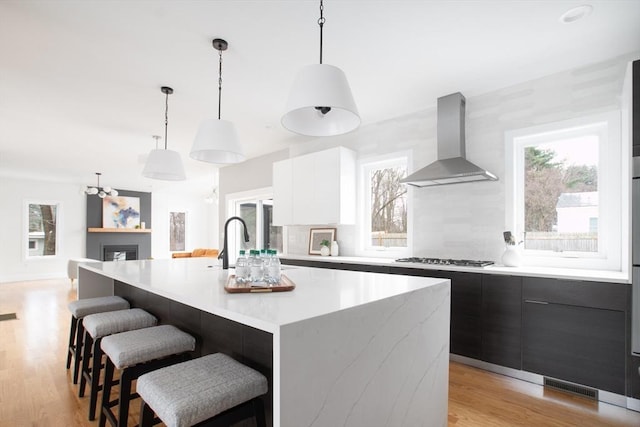 kitchen with light hardwood / wood-style flooring, pendant lighting, stainless steel gas stovetop, a large island, and wall chimney range hood