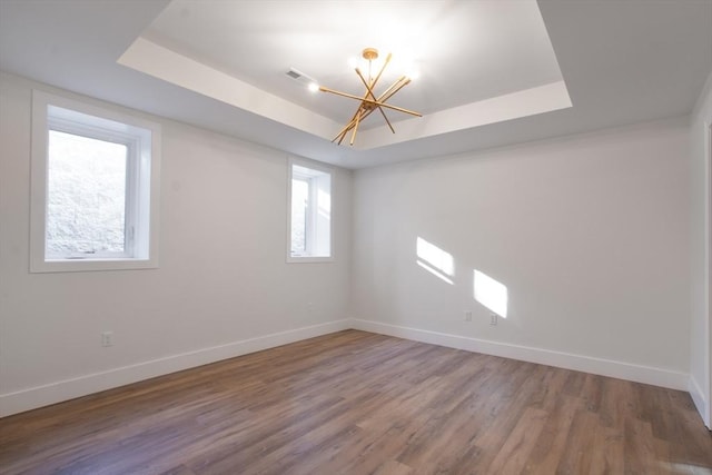 unfurnished room with a chandelier, a raised ceiling, and hardwood / wood-style floors