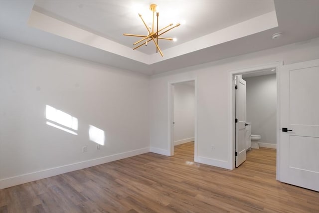 unfurnished bedroom with a notable chandelier, a tray ceiling, and light wood-type flooring