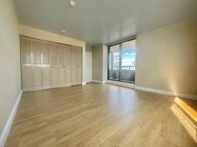 unfurnished bedroom featuring expansive windows, light hardwood / wood-style flooring, and a closet