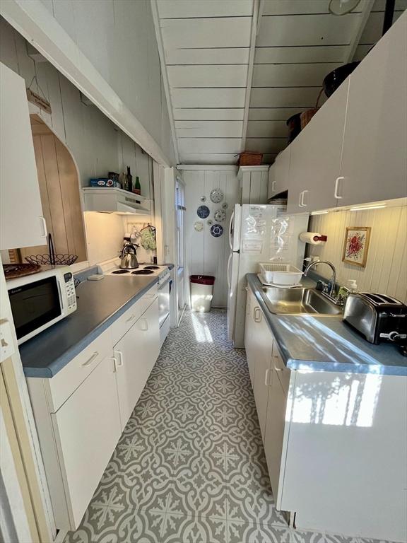 kitchen featuring white cabinetry, wooden walls, white appliances, and sink