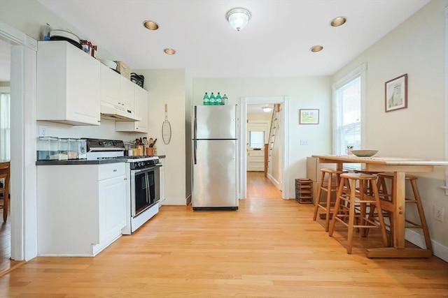 kitchen with light wood finished floors, gas range gas stove, under cabinet range hood, freestanding refrigerator, and white cabinets