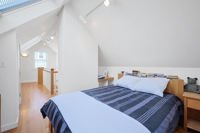 bedroom featuring baseboards, wood finished floors, track lighting, and vaulted ceiling