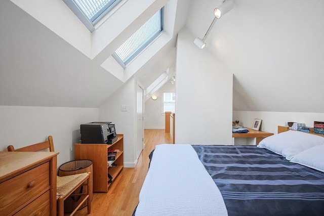 bedroom with light wood finished floors, track lighting, vaulted ceiling with skylight, and baseboards