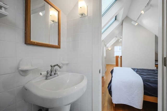 bathroom featuring vaulted ceiling, tile walls, wood finished floors, and a sink