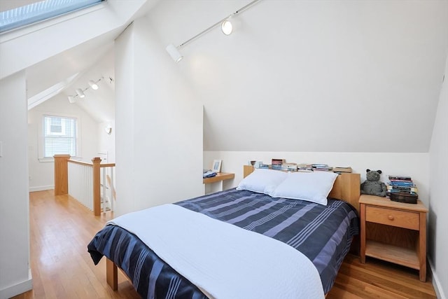 bedroom with rail lighting, lofted ceiling, and wood finished floors