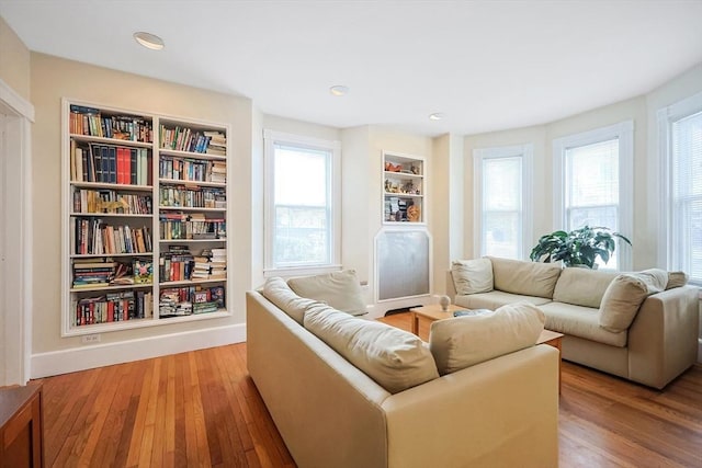 sitting room with built in features, a healthy amount of sunlight, baseboards, and wood-type flooring