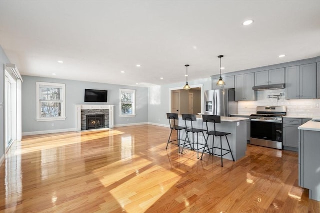 kitchen featuring a breakfast bar, stainless steel appliances, light countertops, gray cabinetry, and a kitchen island