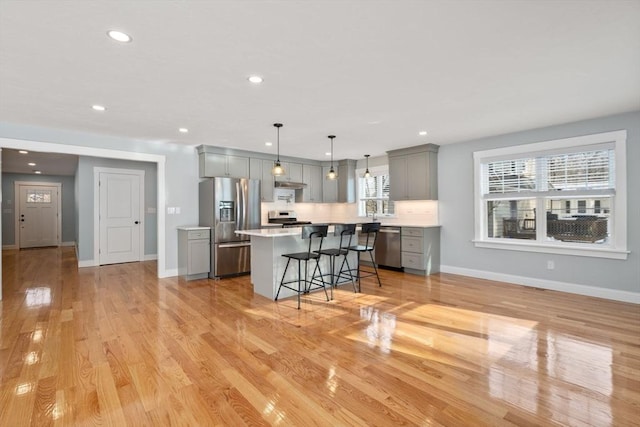 kitchen with decorative light fixtures, a center island, gray cabinets, stainless steel appliances, and light countertops