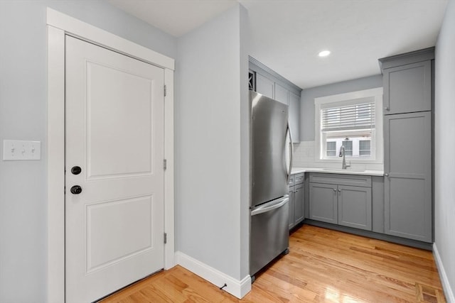 kitchen featuring light wood-style flooring, gray cabinetry, a sink, light countertops, and freestanding refrigerator