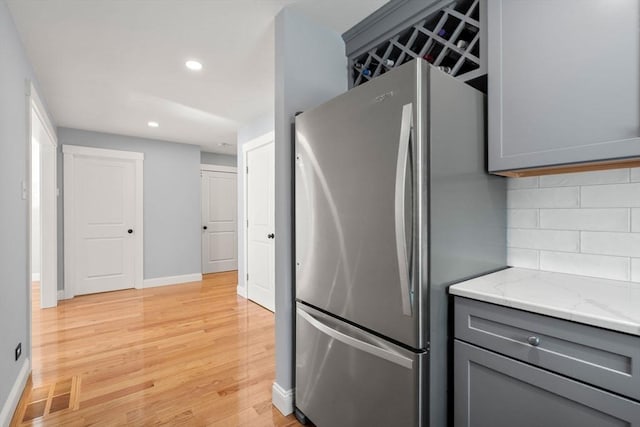 kitchen with light stone counters, tasteful backsplash, gray cabinets, visible vents, and freestanding refrigerator