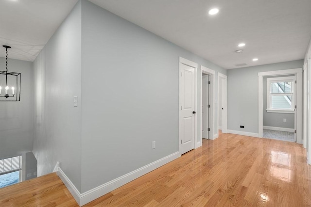 hallway with recessed lighting, baseboards, light wood finished floors, and an inviting chandelier