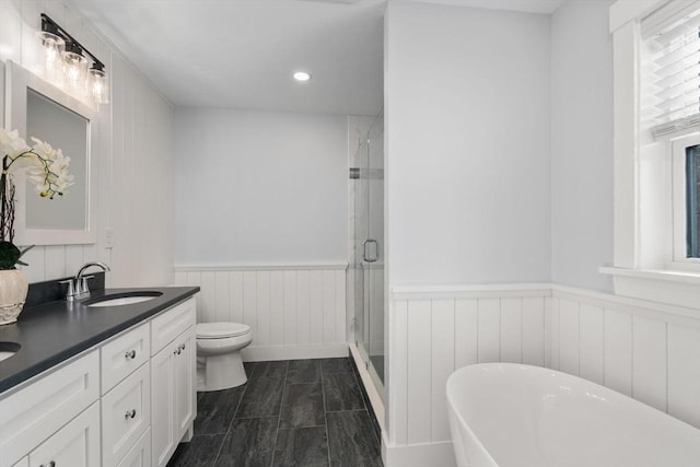 full bath featuring toilet, a wainscoted wall, a sink, a soaking tub, and a stall shower