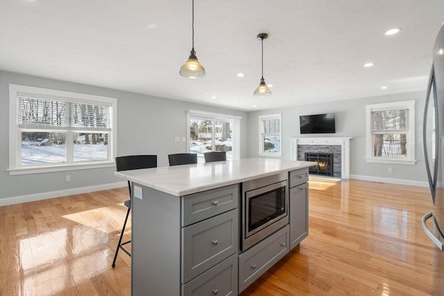 kitchen with pendant lighting, stainless steel microwave, gray cabinetry, light wood-style floors, and a kitchen bar