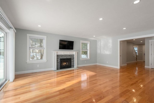 unfurnished living room with recessed lighting, a fireplace with flush hearth, a wealth of natural light, and light wood-style floors