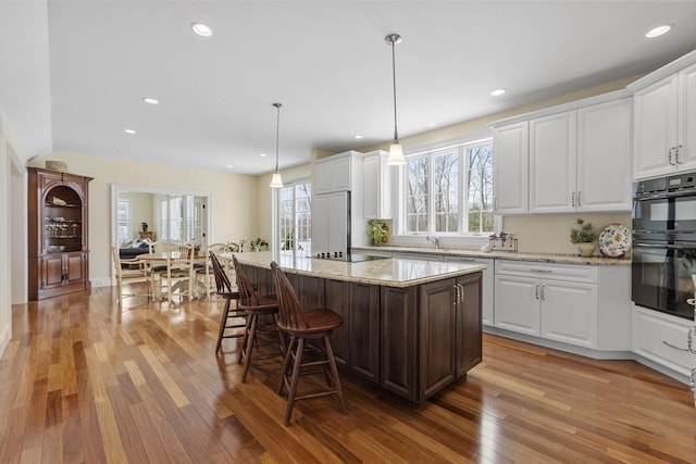 kitchen featuring a kitchen island, white cabinetry, hanging light fixtures, and light stone counters