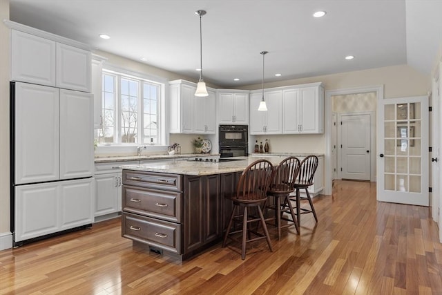 kitchen with hanging light fixtures, white cabinetry, light stone counters, a kitchen bar, and a center island