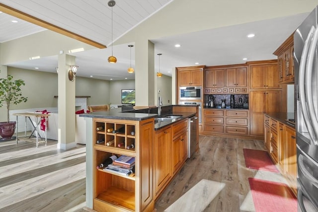 kitchen featuring appliances with stainless steel finishes, pendant lighting, decorative backsplash, a kitchen island with sink, and light hardwood / wood-style floors