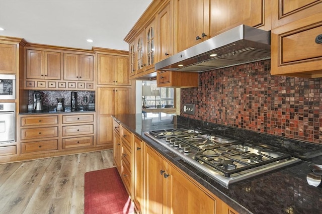 kitchen featuring tasteful backsplash, wall oven, exhaust hood, stainless steel gas stovetop, and light wood-type flooring