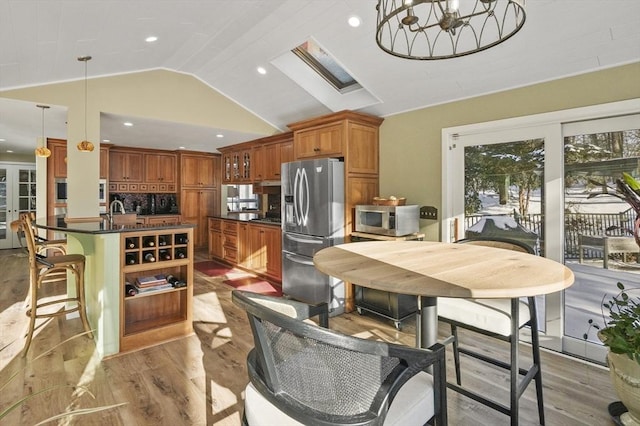 dining space featuring lofted ceiling with skylight, a chandelier, and light hardwood / wood-style flooring