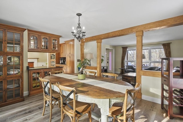 dining space featuring decorative columns, a notable chandelier, and light hardwood / wood-style flooring