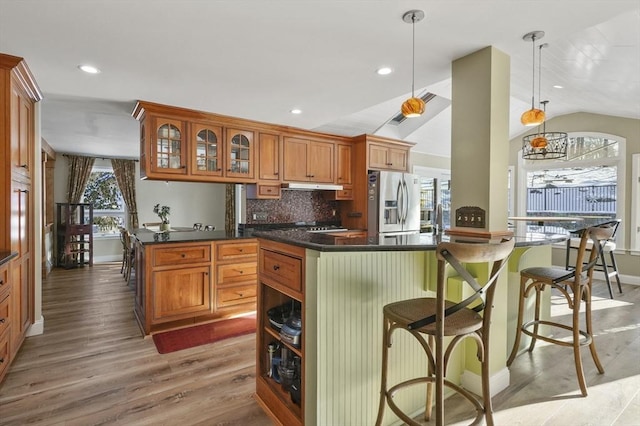 kitchen with vaulted ceiling, decorative light fixtures, stainless steel fridge, decorative backsplash, and light hardwood / wood-style flooring