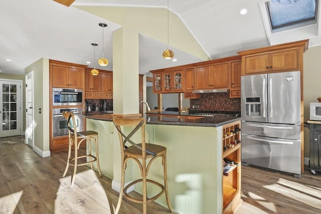 kitchen with appliances with stainless steel finishes, decorative light fixtures, lofted ceiling, backsplash, and a kitchen breakfast bar